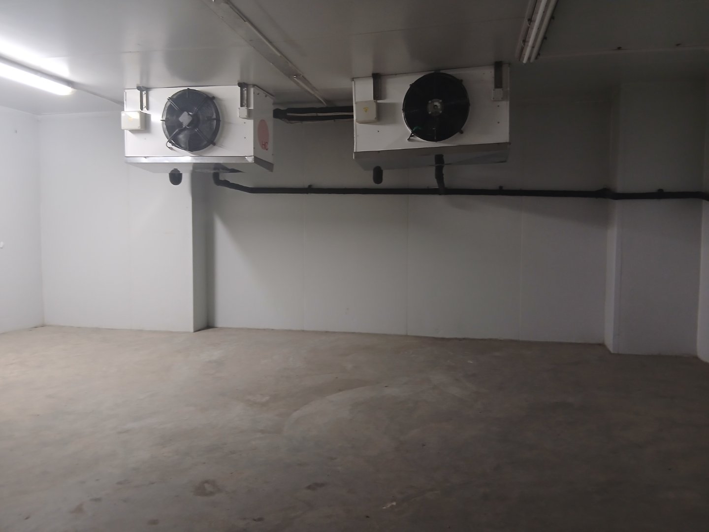 Industrial Cooling Units in Warehouse Two industrial cooling units installed on the ceiling of a warehouse with white walls and concrete floor.