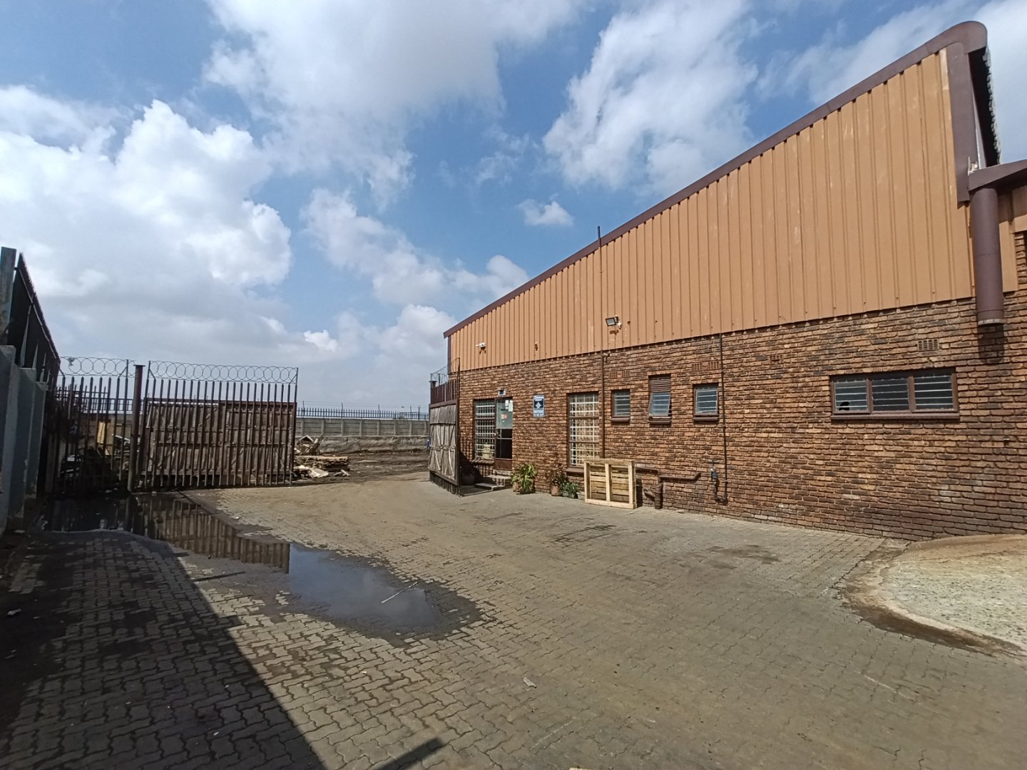 Industrial warehouse with brick and metal exterior in Alrode, showcasing a spacious outdoor area and clear sky, suitable for manufacturing or storage.