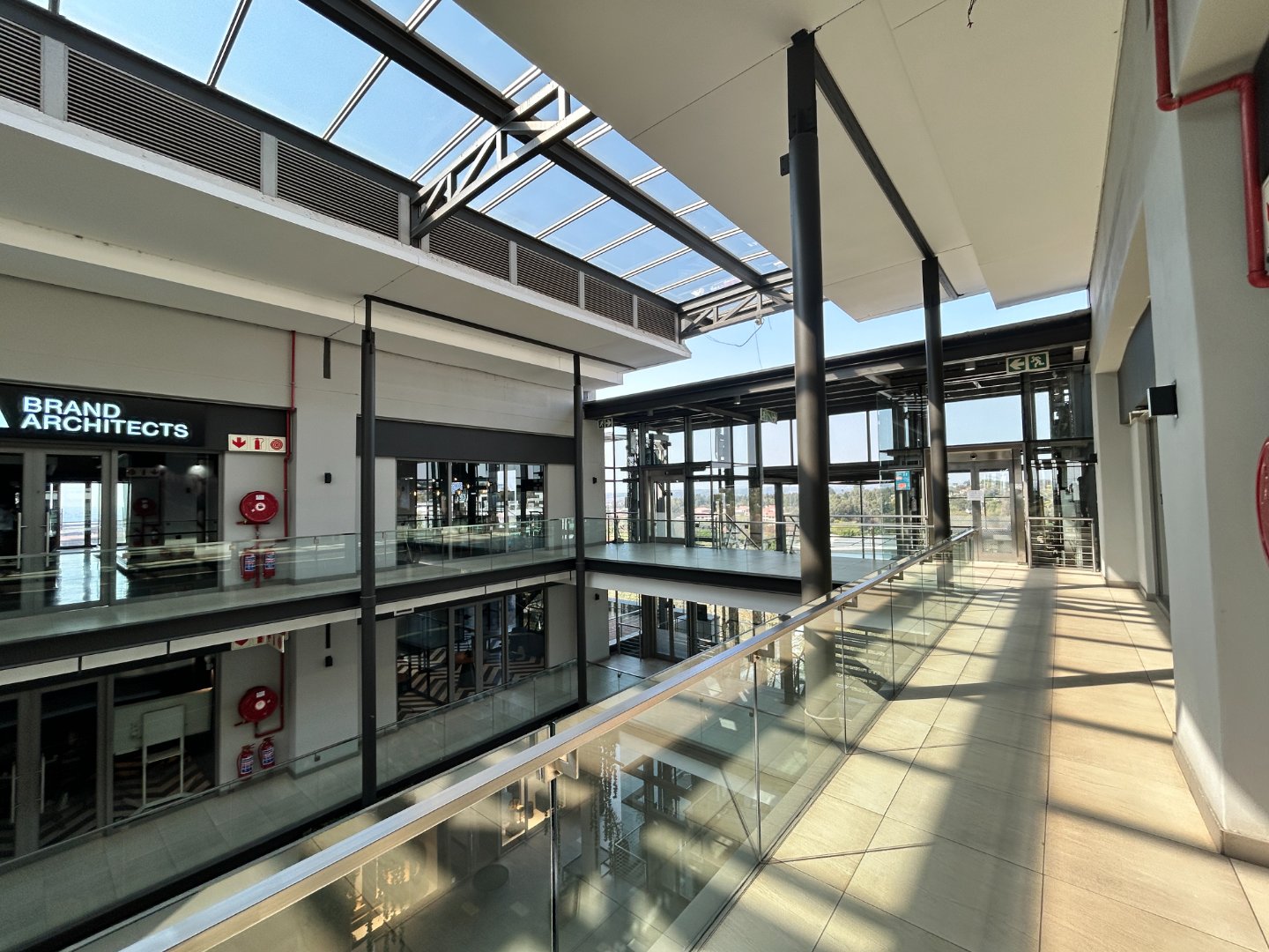 Bright, spacious office corridor with glass walls and natural lighting, showcasing contemporary architecture and open-plan design.