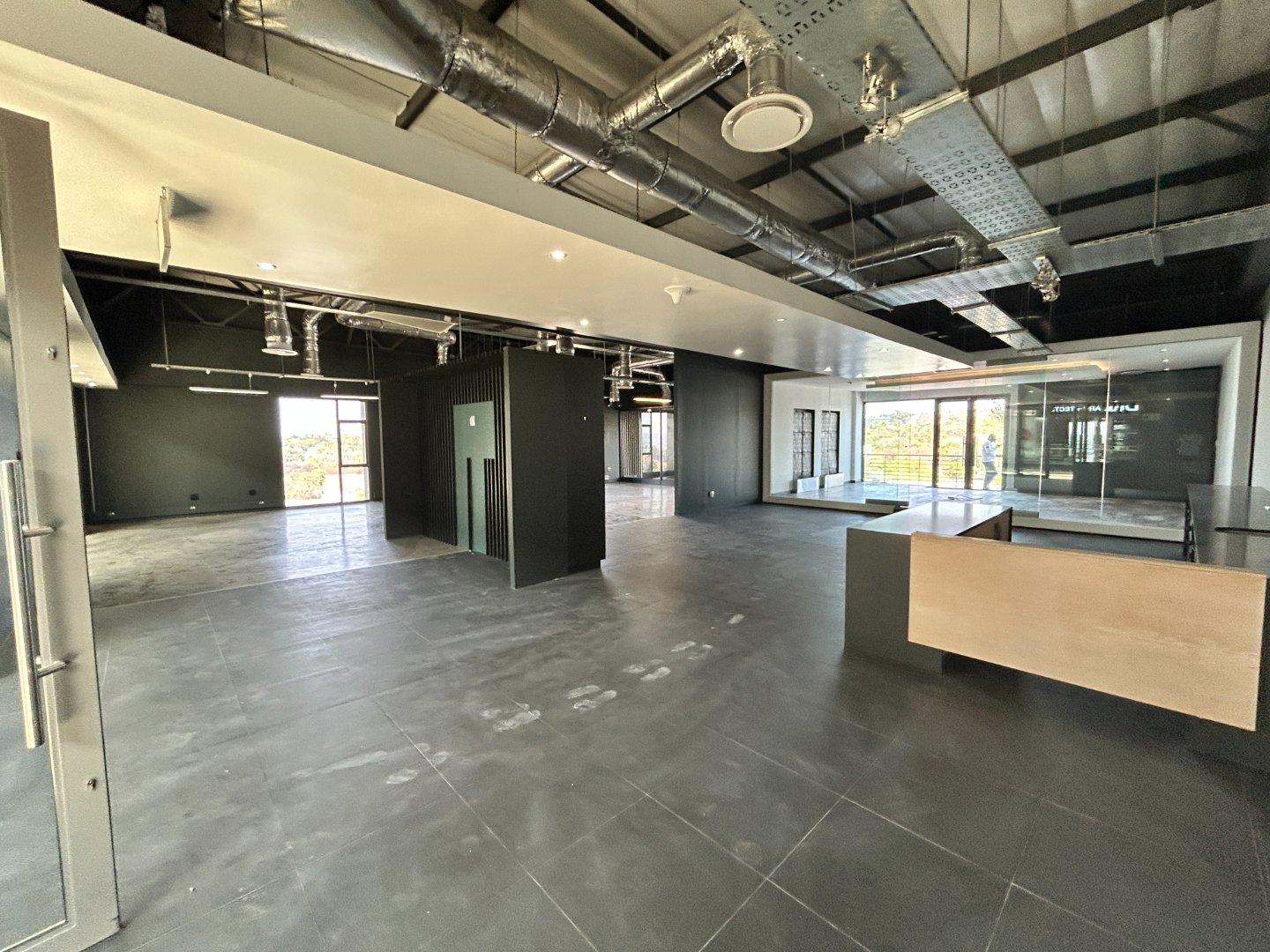 Spacious modern office interior with black walls, exposed ductwork, large windows, and a reception desk, showcasing a professional workspace environment.