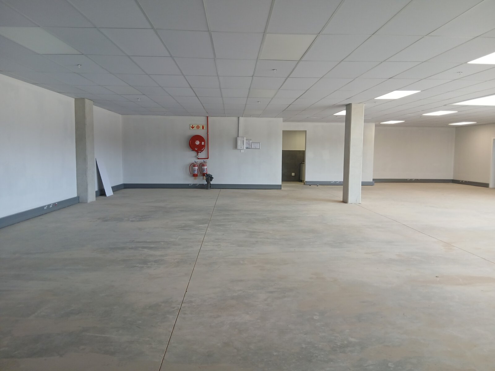 Interior view of a large, empty warehouse with a clean concrete floor, white walls, and a suspended ceiling, showcasing modern office and storage space.