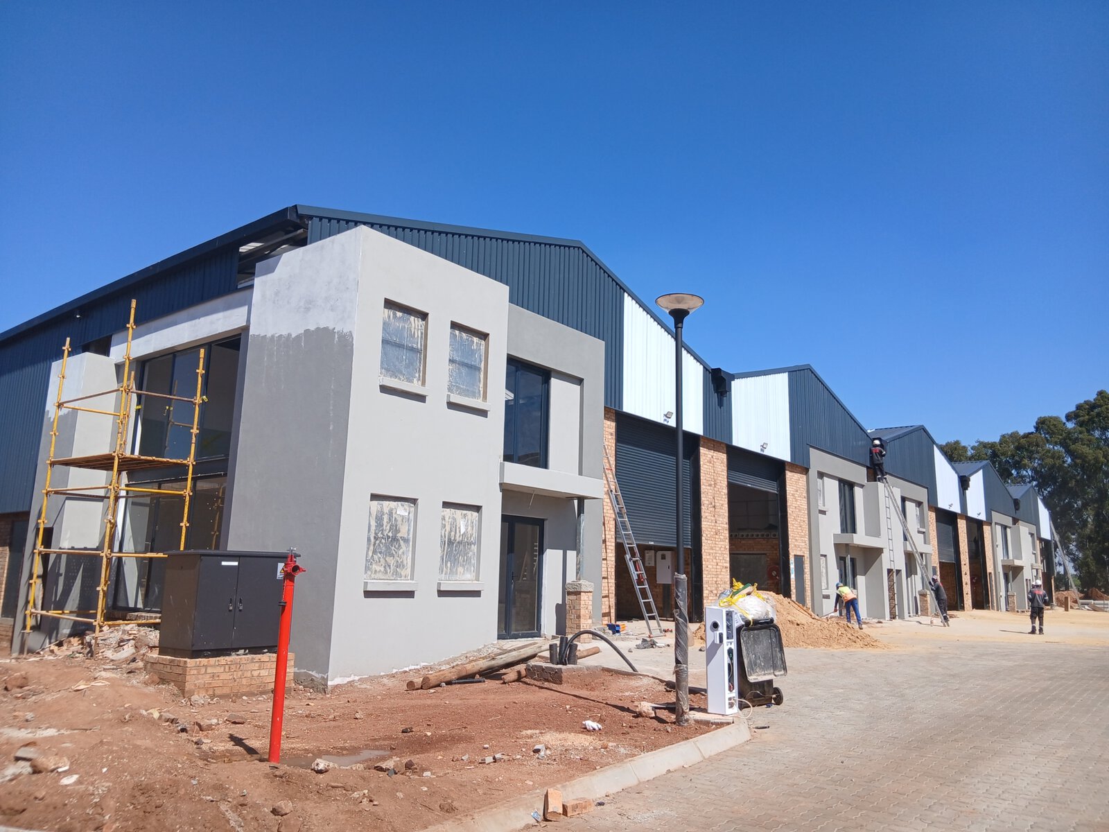 Newly constructed office and warehouse buildings with modern design, under construction with scaffolding and construction equipment present.
