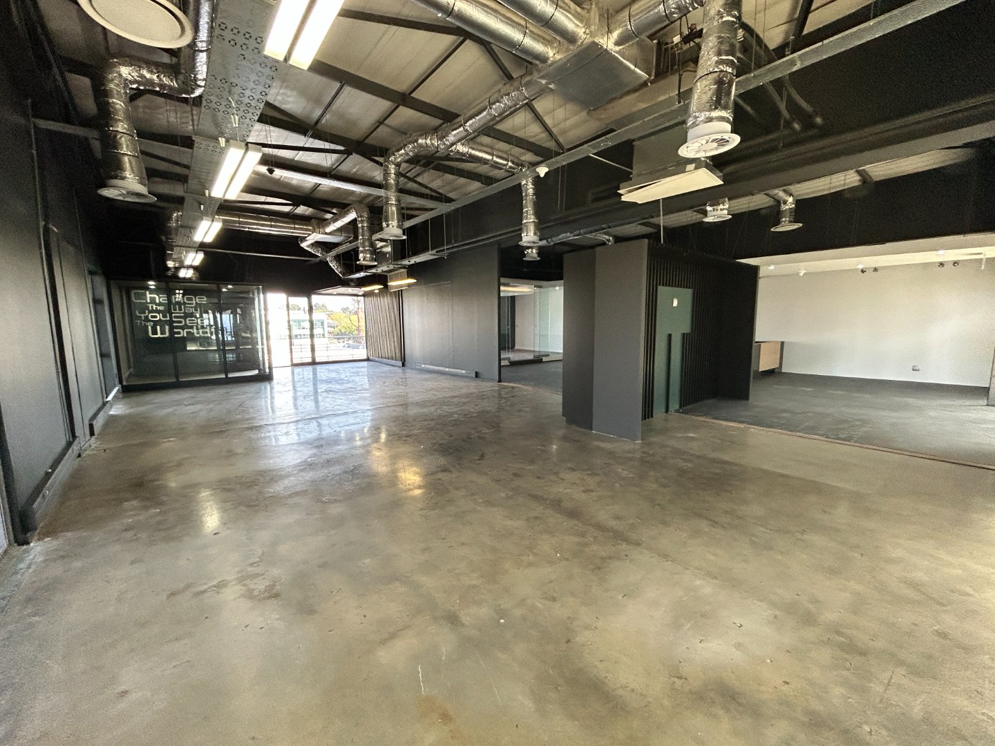 Spacious modern office with polished concrete floors, exposed ductwork, and large windows for natural light, suitable for corporate or creative work environments.